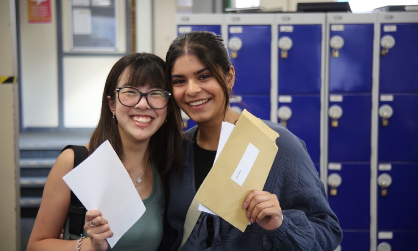 Photo of two students holding their results envelopes and smiling