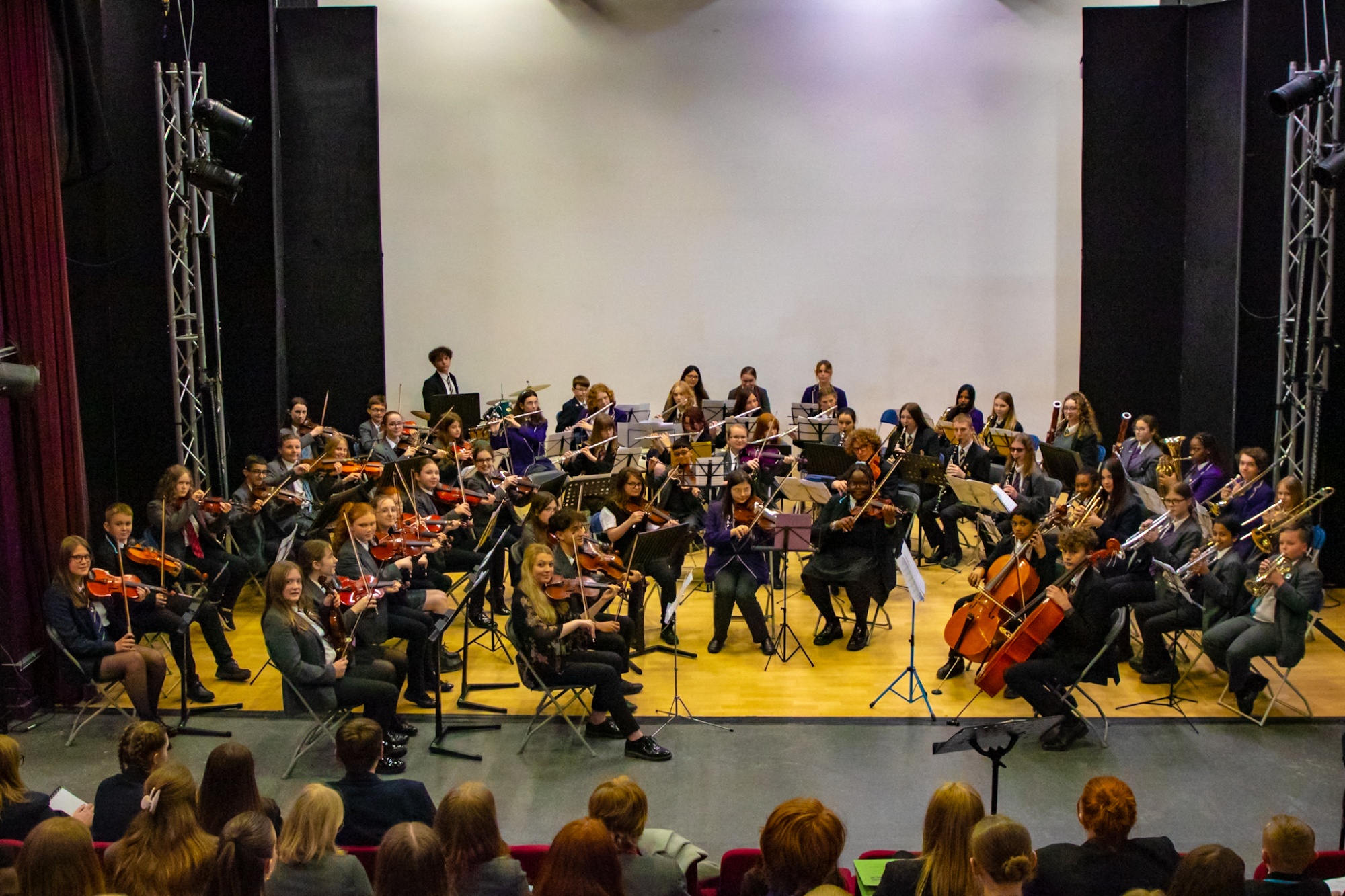A group of young musicians sit in orchestra formation 