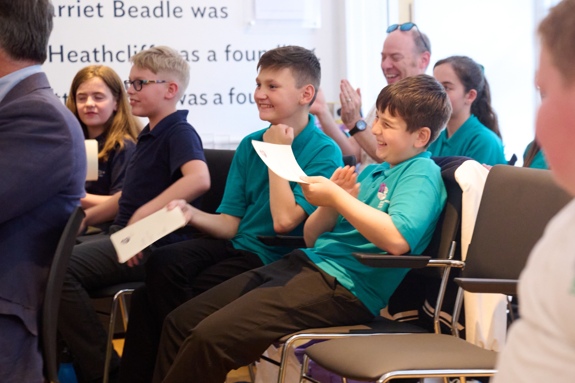 A group of young people in school uniform applaud and smile