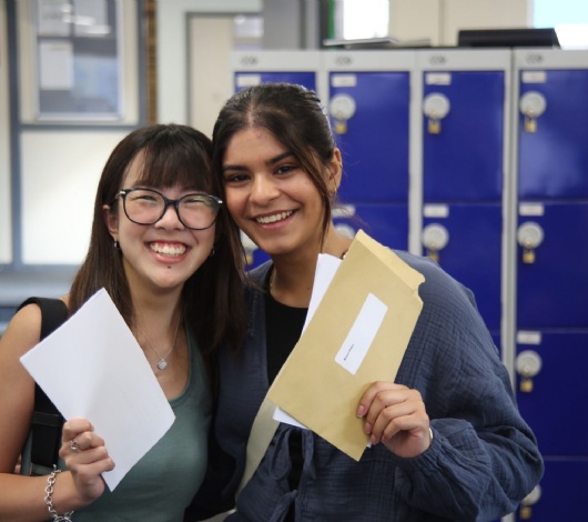 Photo of two students holding their results envelopes and smiling